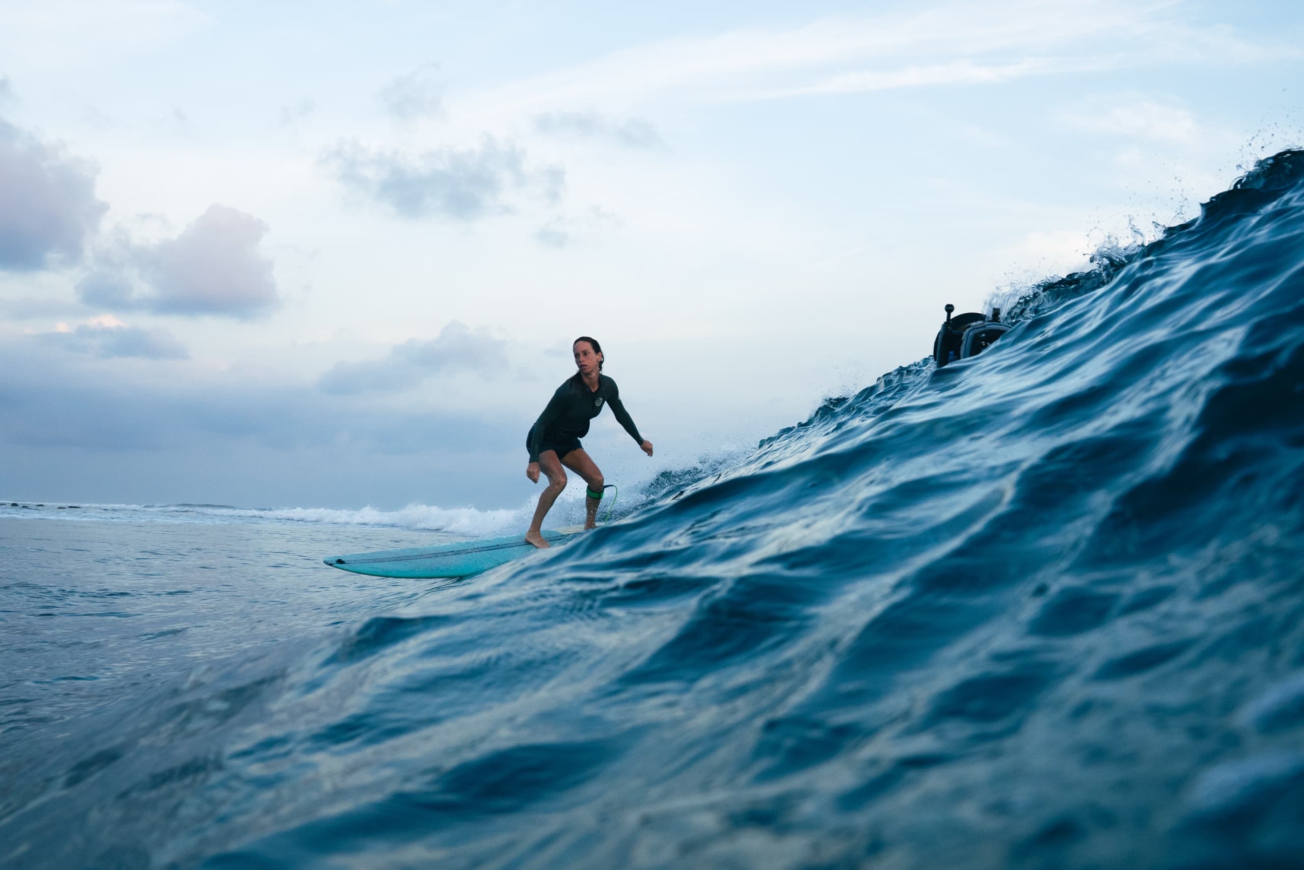 Surfer in a black rash vest riding a teal board along a blue wave